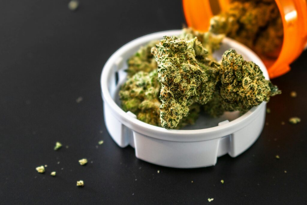 Close-up of cannabis buds spilling from a prescription container, isolated on black background.